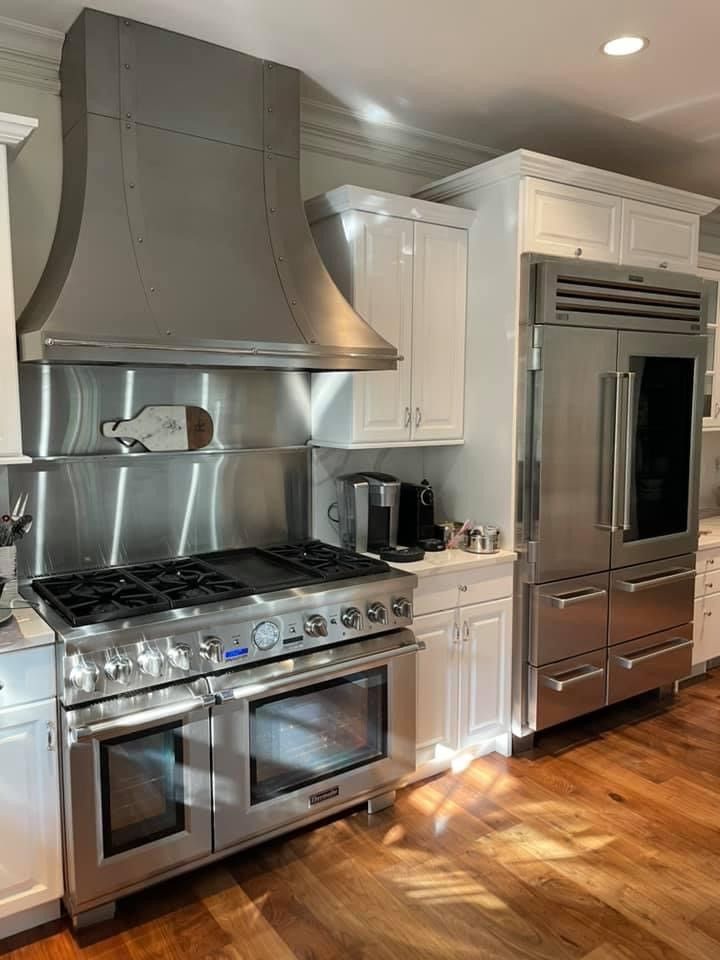 Stainless steel kitchen with stove, hood, fridge, white cabinets, and hardwood floor.