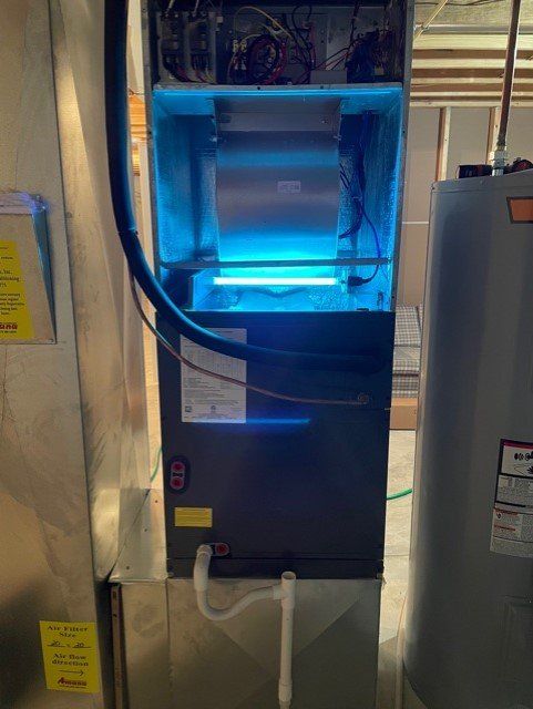 A blue UV light illuminates an HVAC unit with a water heater nearby, in a basement setting.