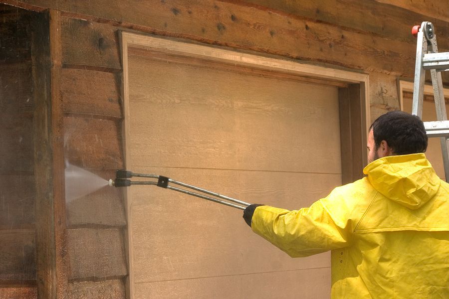 Person in yellow raincoat pressure washing wooden structure.