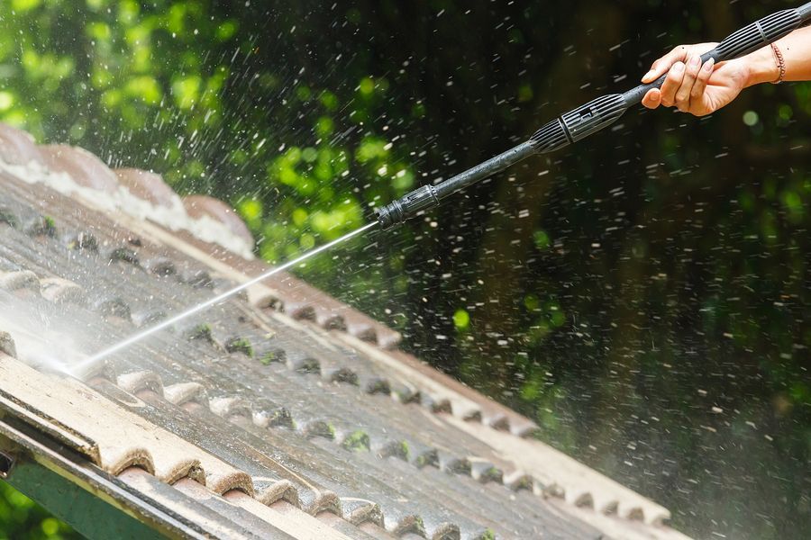 Person power washing a tiled roof.