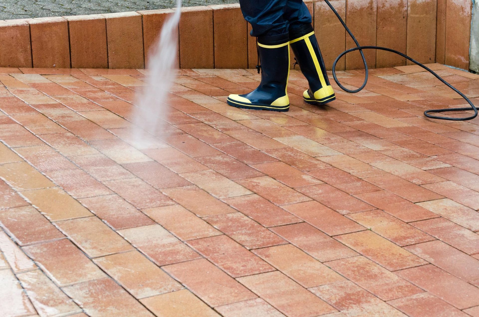 Person power washing brick patio.