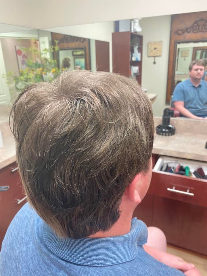 Person with brown, textured hair in a salon, a stylist reflected in the mirror.