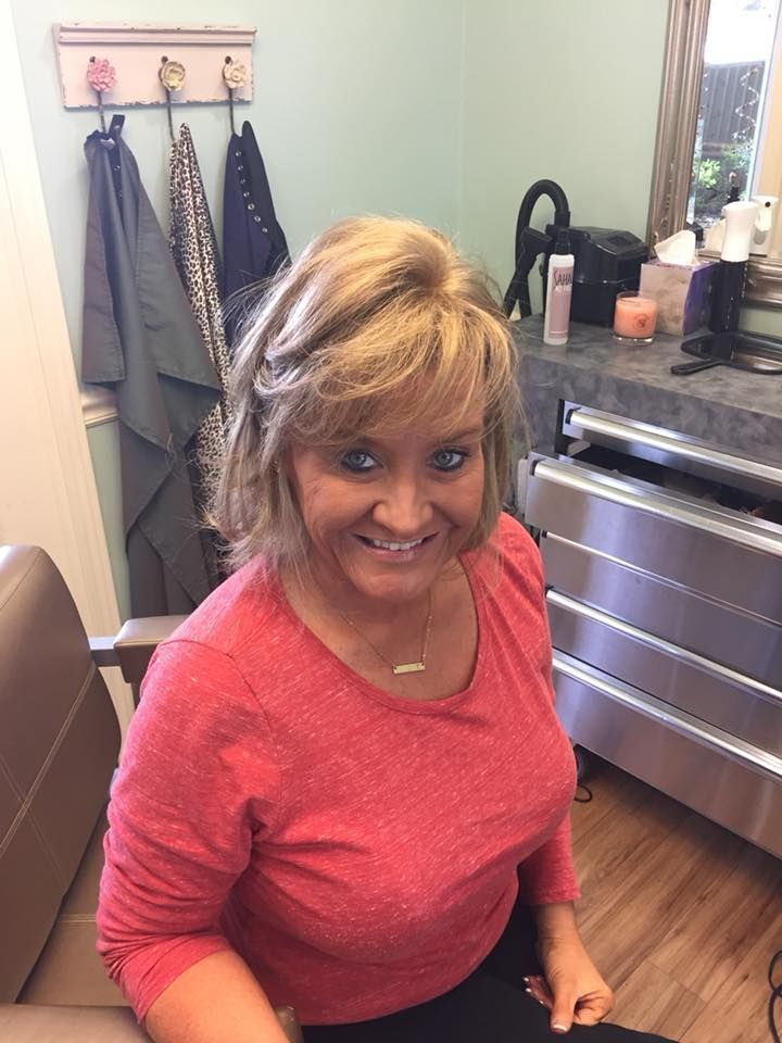 Woman with blonde hair, wearing a pink shirt, smiling in a salon.