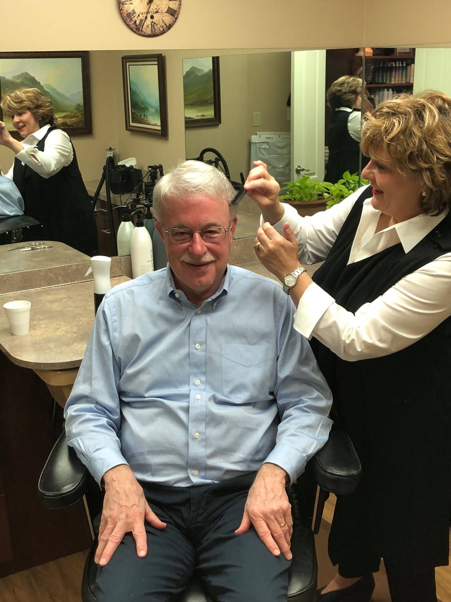A man in a blue shirt gets a haircut from a woman in a salon.