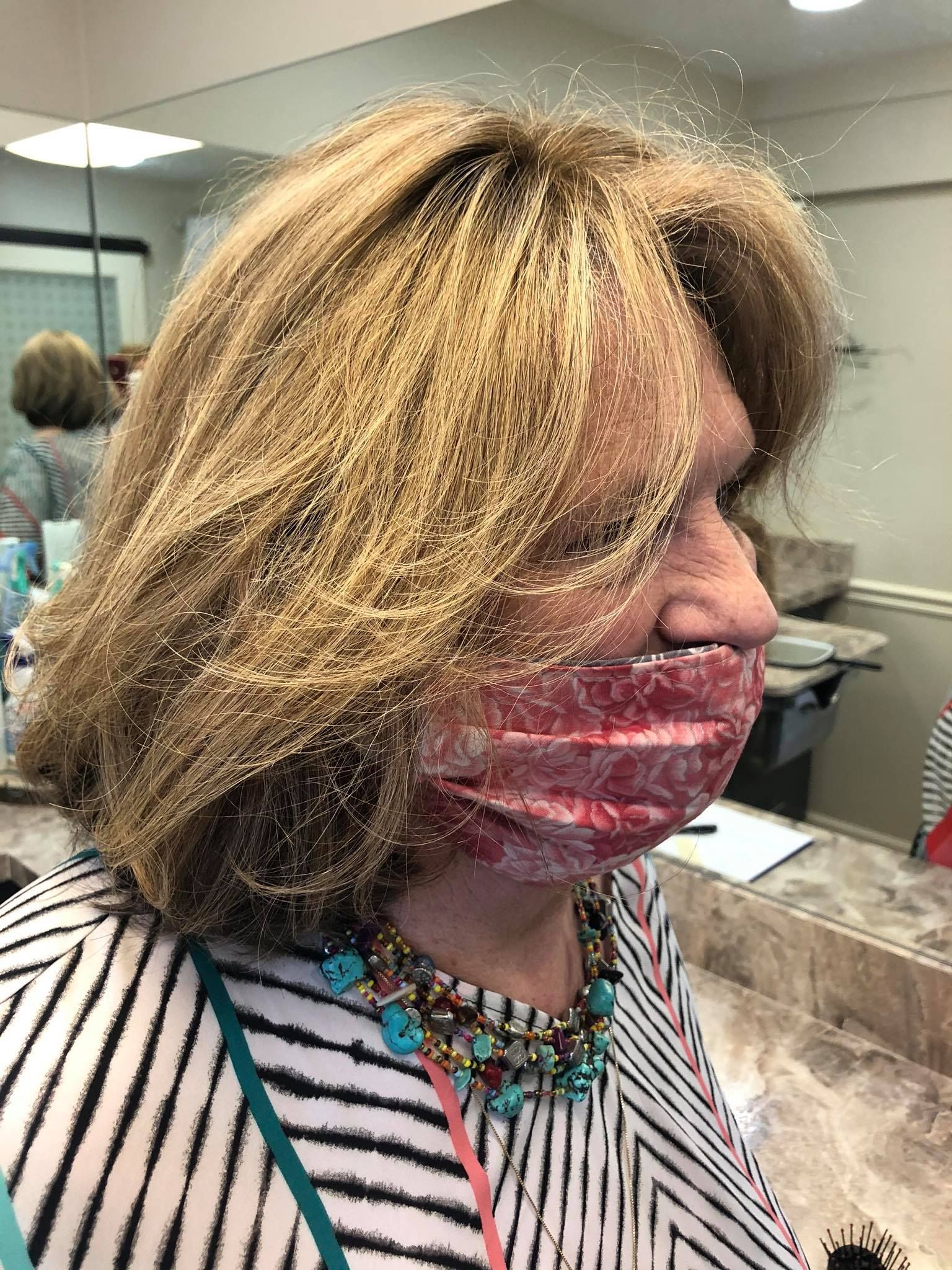 Woman with blonde hair wearing a striped shirt and a red patterned face mask.
