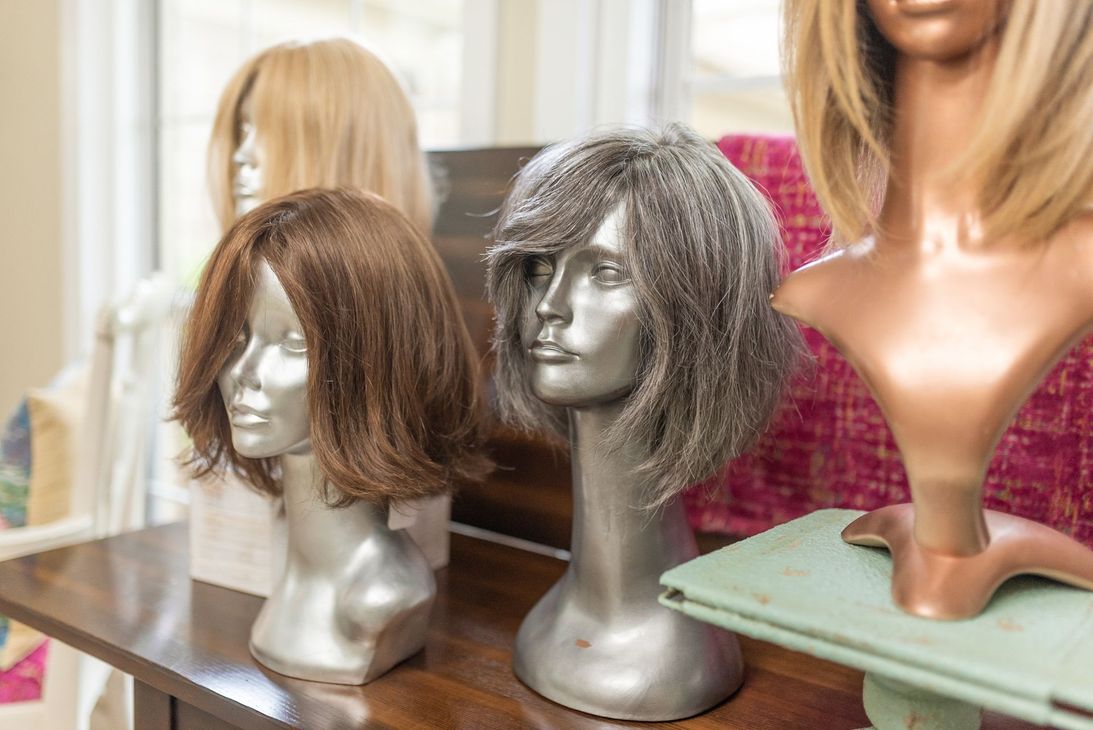 Wigs on mannequin heads, various colors: brown, gray, blonde. Displayed on a wooden table.