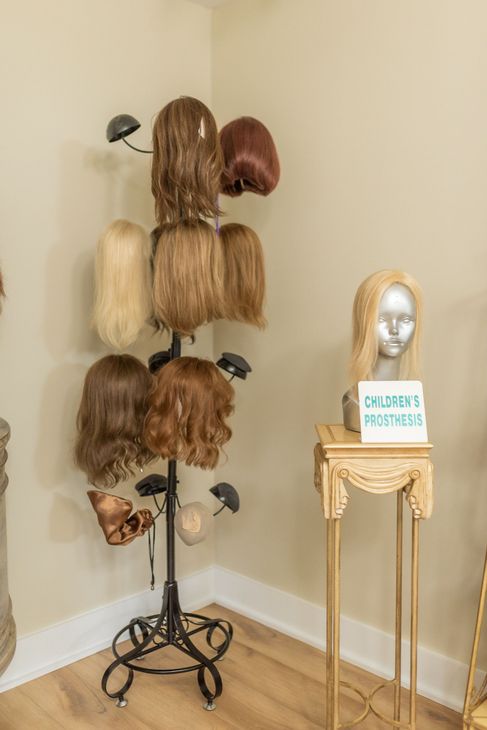 Wigs displayed on a black tiered stand and mannequin head on a decorative table in a room.