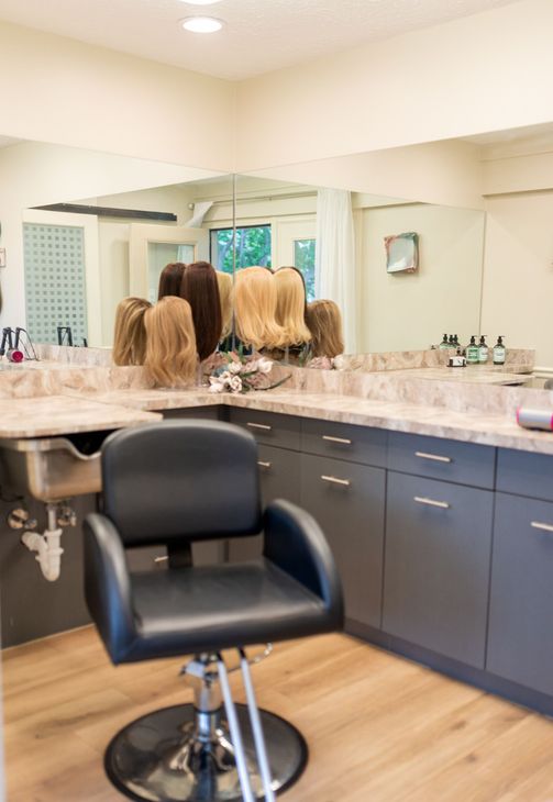 Hair salon: black chair, wigs on display, gray cabinets, large mirror.