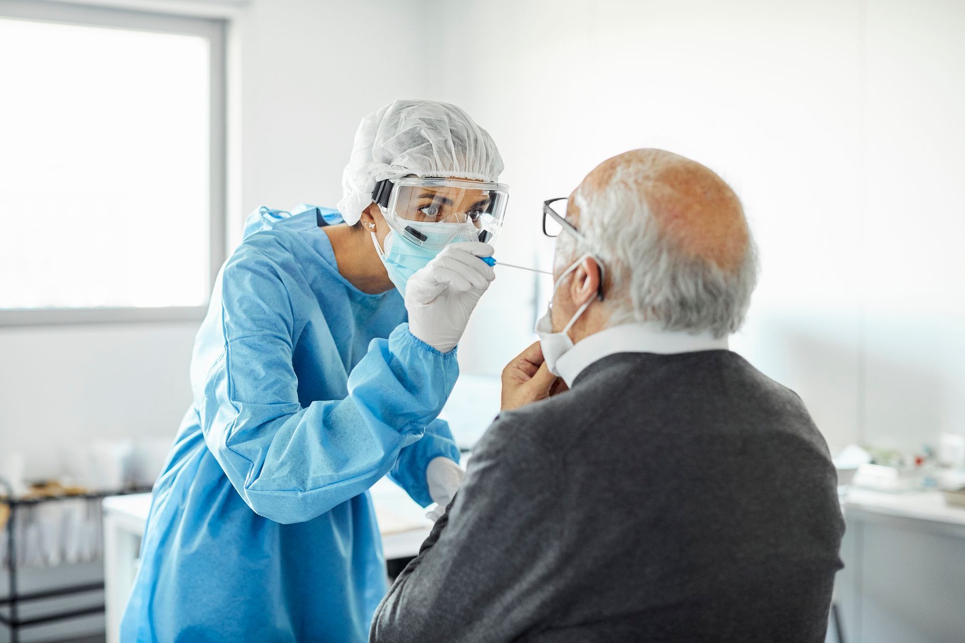 A doctor is taking a sample from an elderly man 's nose.