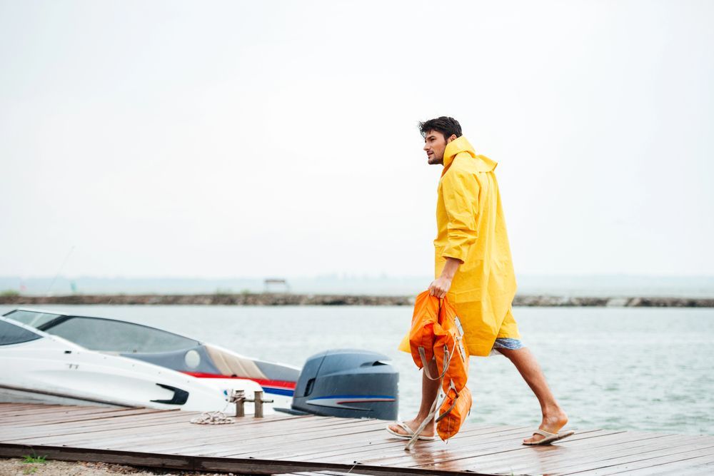 Un hombre con un impermeable amarillo camina hacia un barco en un muelle.