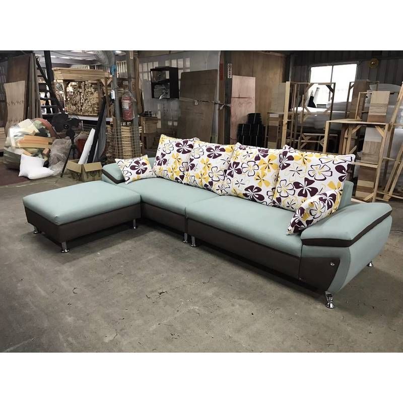 A large sectional couch with floral pillows is sitting in a warehouse.