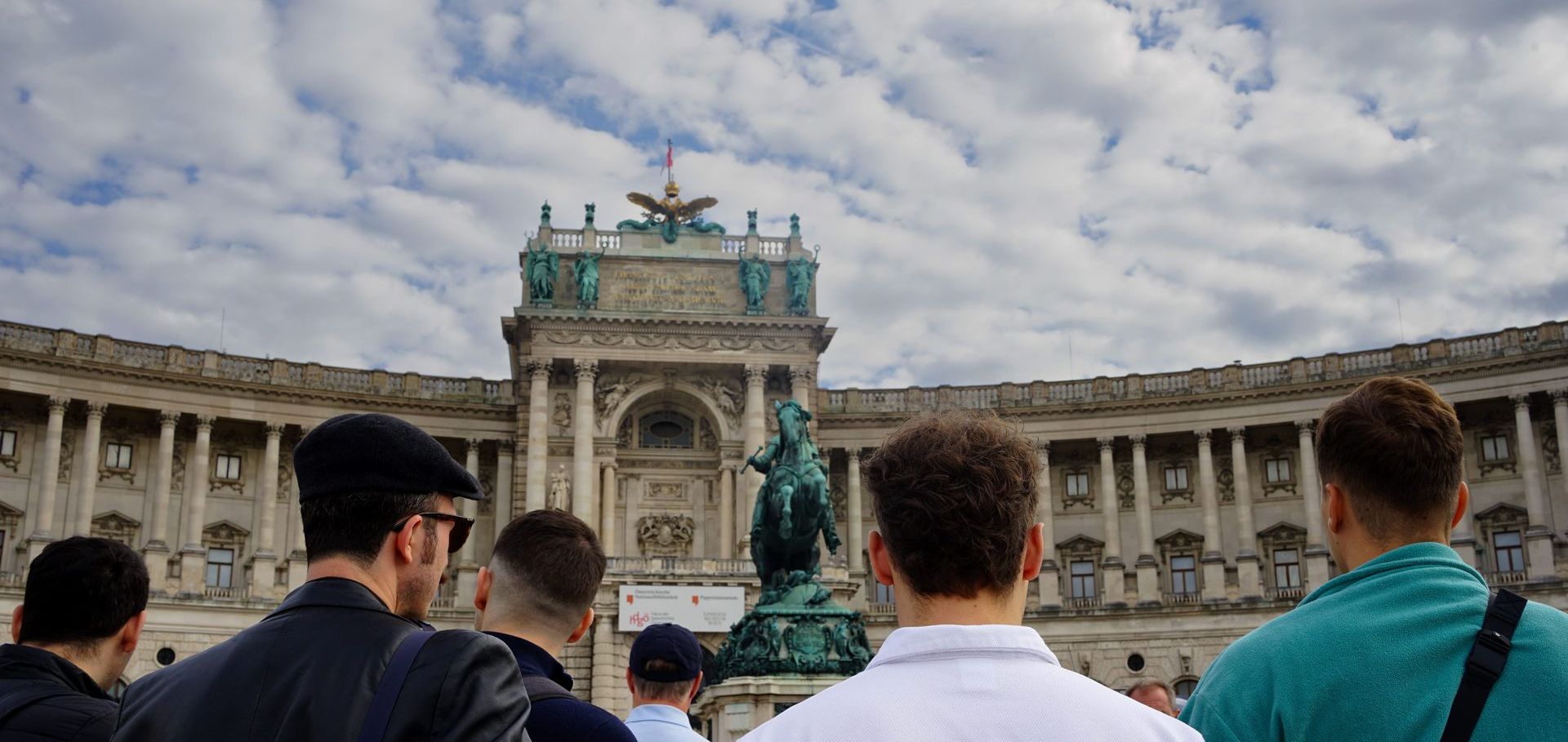Tourists visiting Hofburg Palace Vienna with view of the Neue Burg wing and statue in the foreground