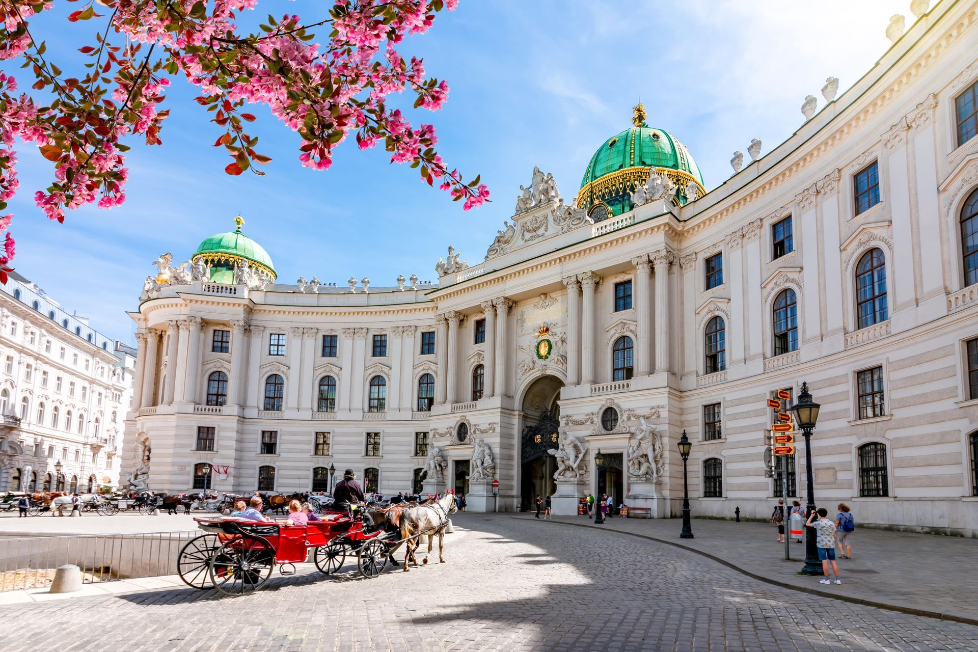 Front view of the St. Michael's Wing at Hofburg Palace Vienna with tourists walking and horse-drawn 
