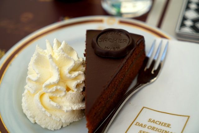 A slice of original Sachertorte with whipped cream served on a white plate at Café Sacher in Vienna
