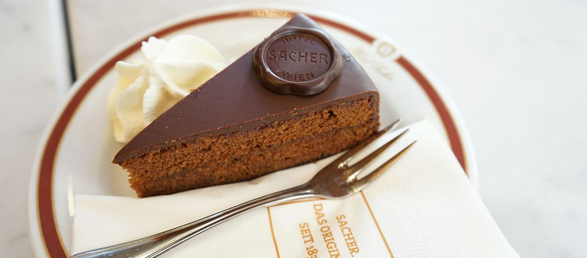 Original Sachertorte served at Café Sacher in Vienna with whipped cream and fork on plate