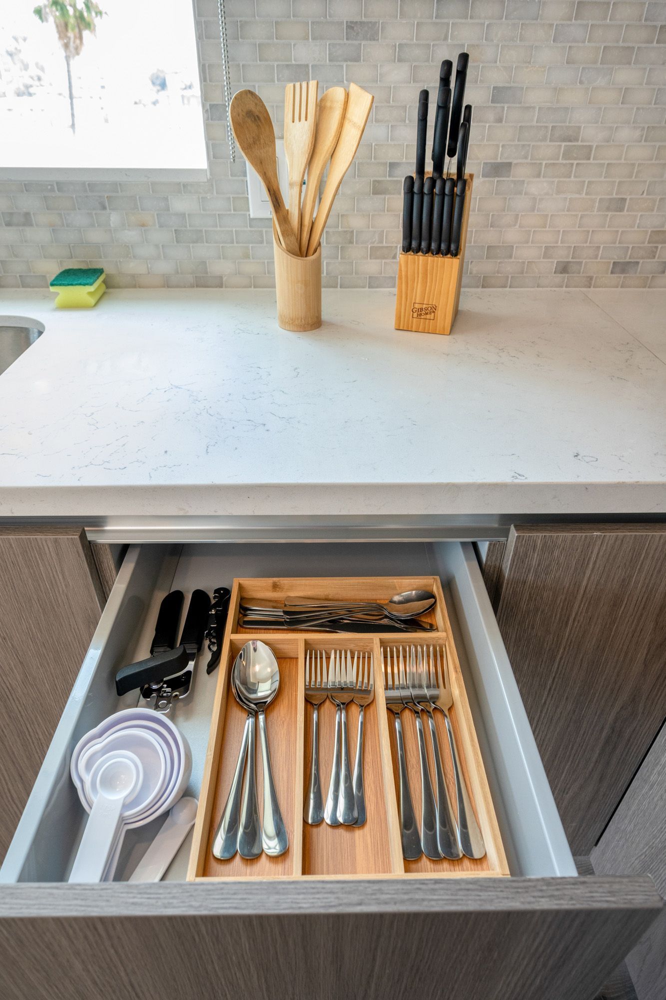 A kitchen drawer filled with silverware and measuring cups.
