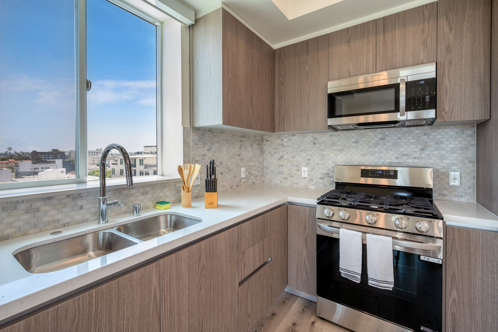 A kitchen with a sink , stove , microwave and window.