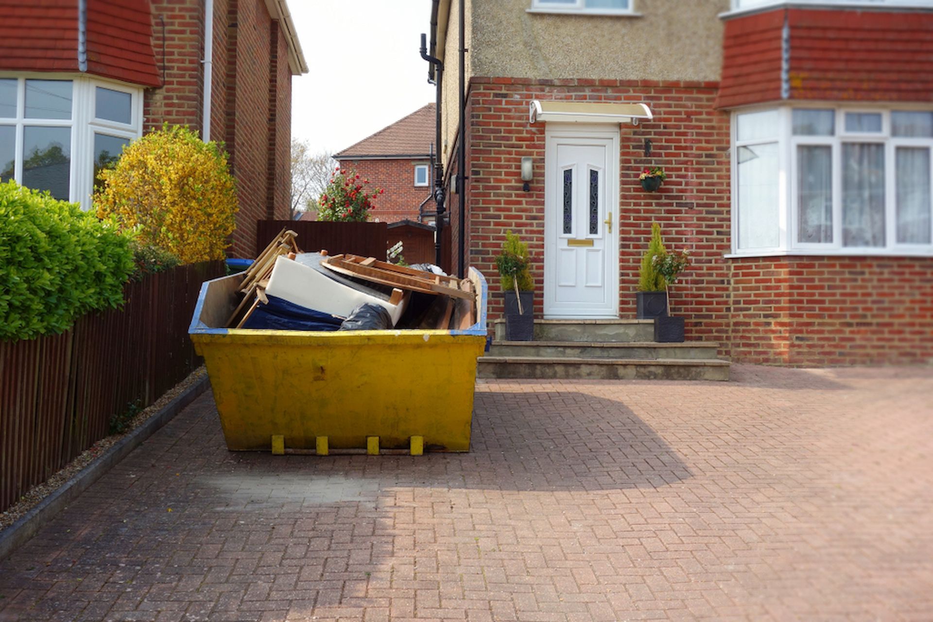 A brick house with a yellow skip full of rubbish in front