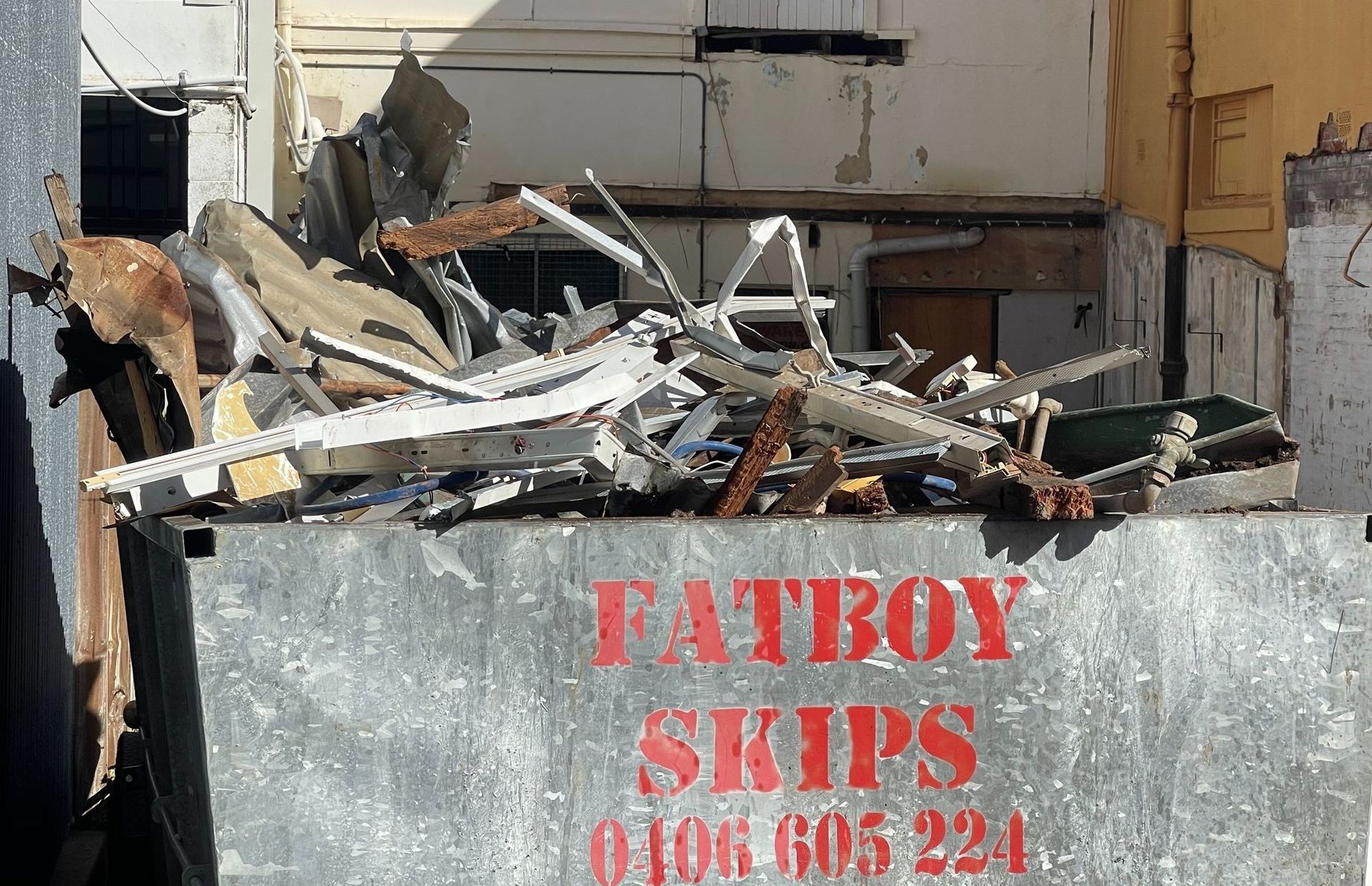 A metallic, overfilled skip bin with a red logo reading 'Fatboy Skips'.