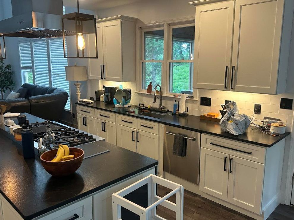 Bright modern kitchen with white cabinets, black countertops, island, sink, and window view