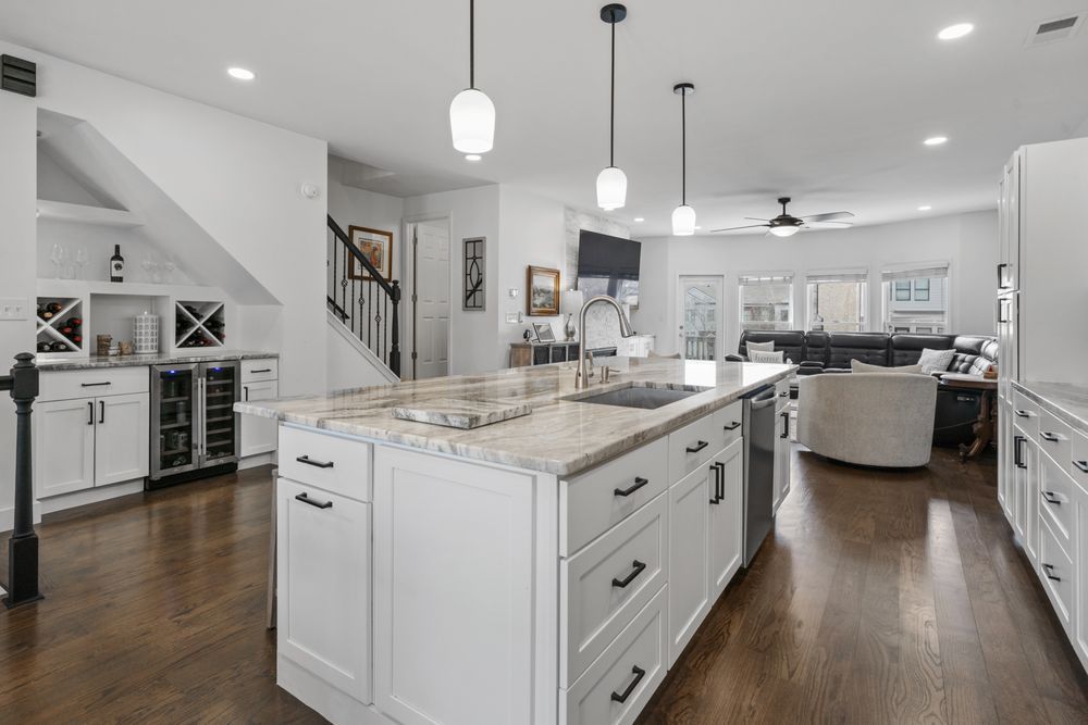 Bright modern kitchen with white cabinets, large island, pendant lights, and dark wood floors