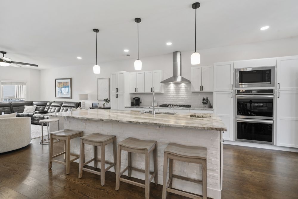 Bright modern kitchen with white cabinets, island stools, pendant lights, and built-in double oven