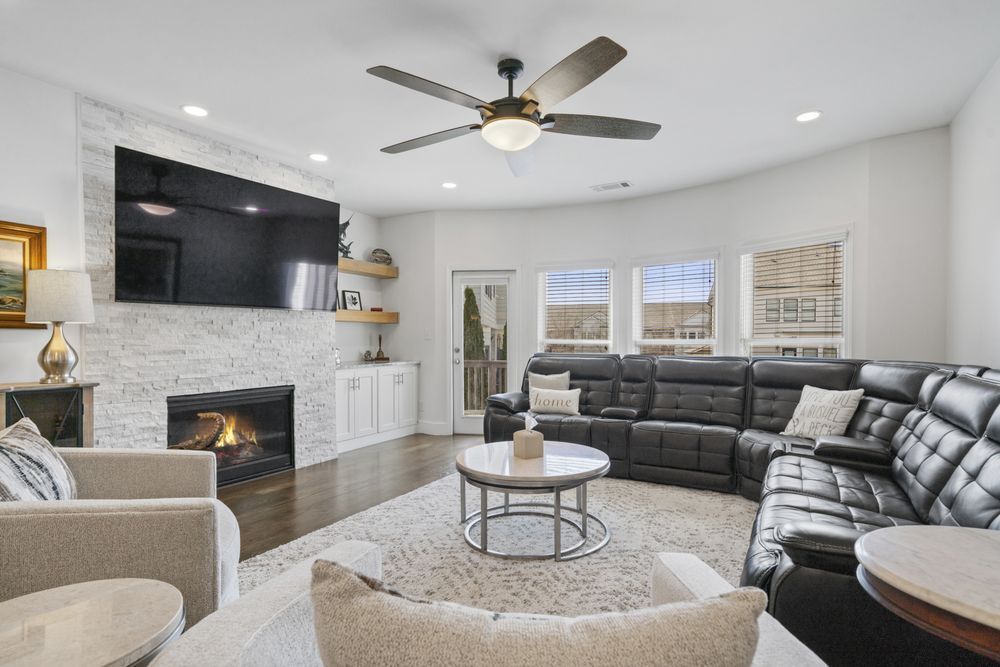 Bright living room with black sectional, fireplace, ceiling fan, and large windows.