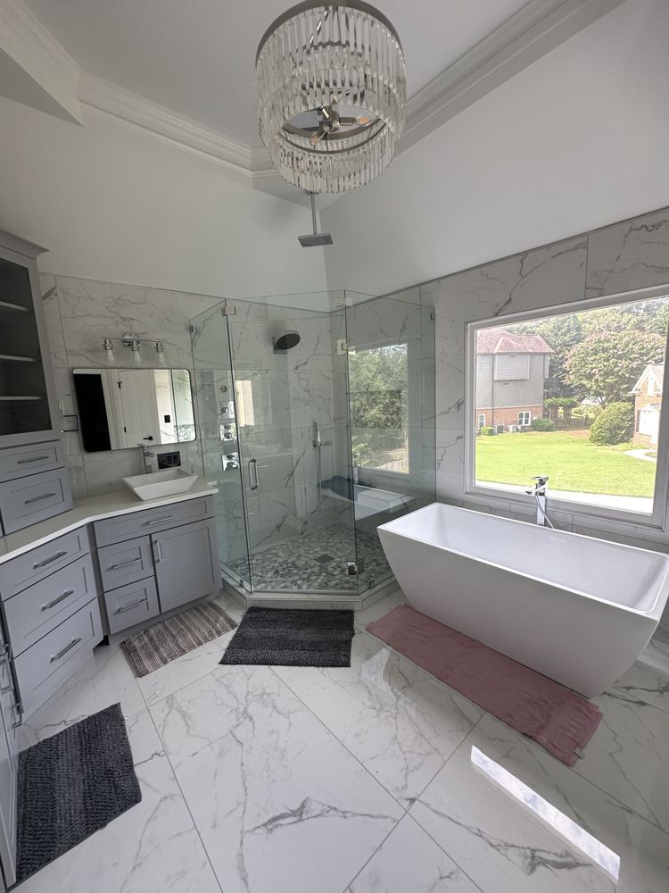 Modern bathroom with marble tile, glass shower, chandelier, and a large window overlooking a yard