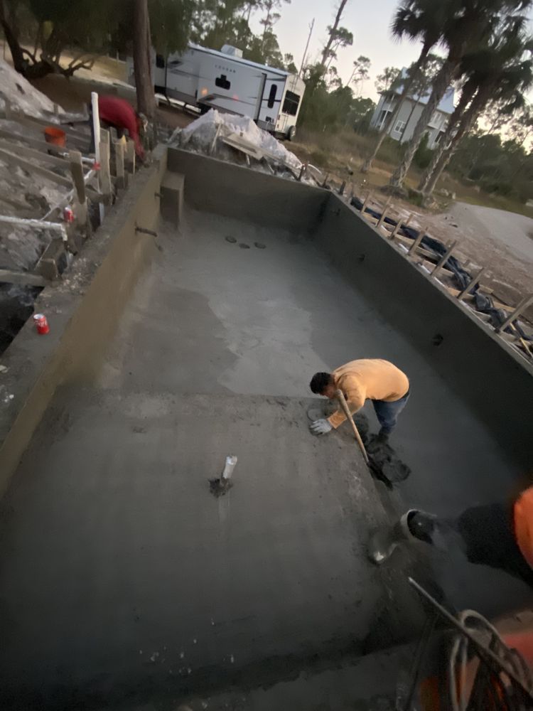 Worker smoothing wet concrete inside a large rectangular pool under construction