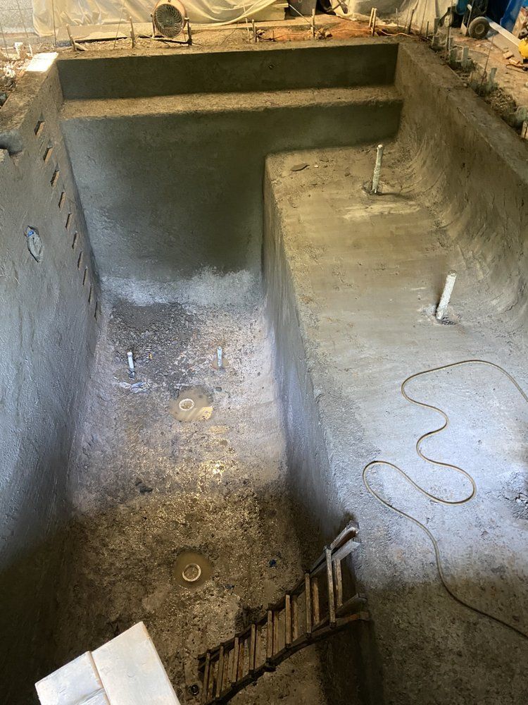 Empty concrete pool under construction with steep sloped floor and stairs at one end.