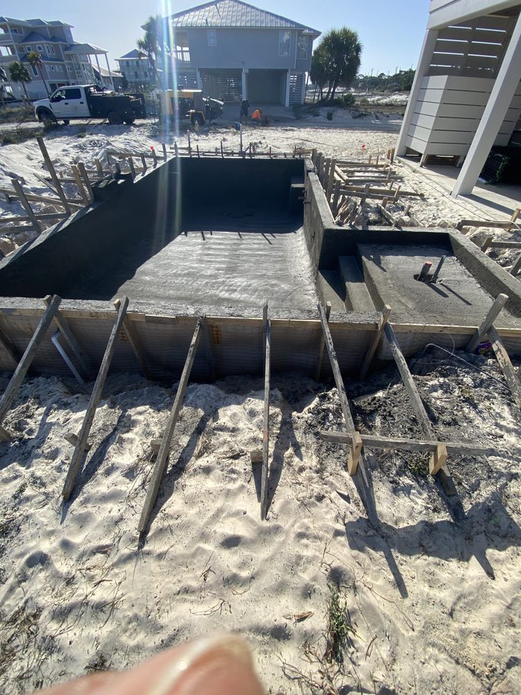 Beachside concrete pool under construction with rebar, wooden formwork, and a house in the background