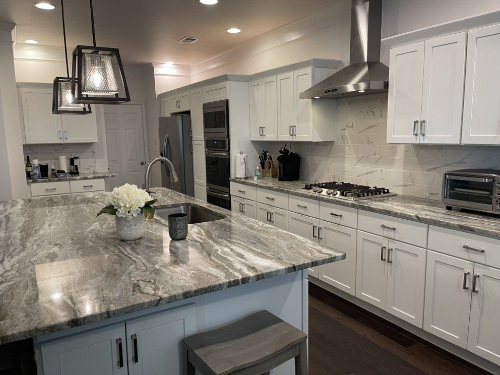 Bright modern kitchen with white cabinets, marble island, stainless appliances, and pendant lights