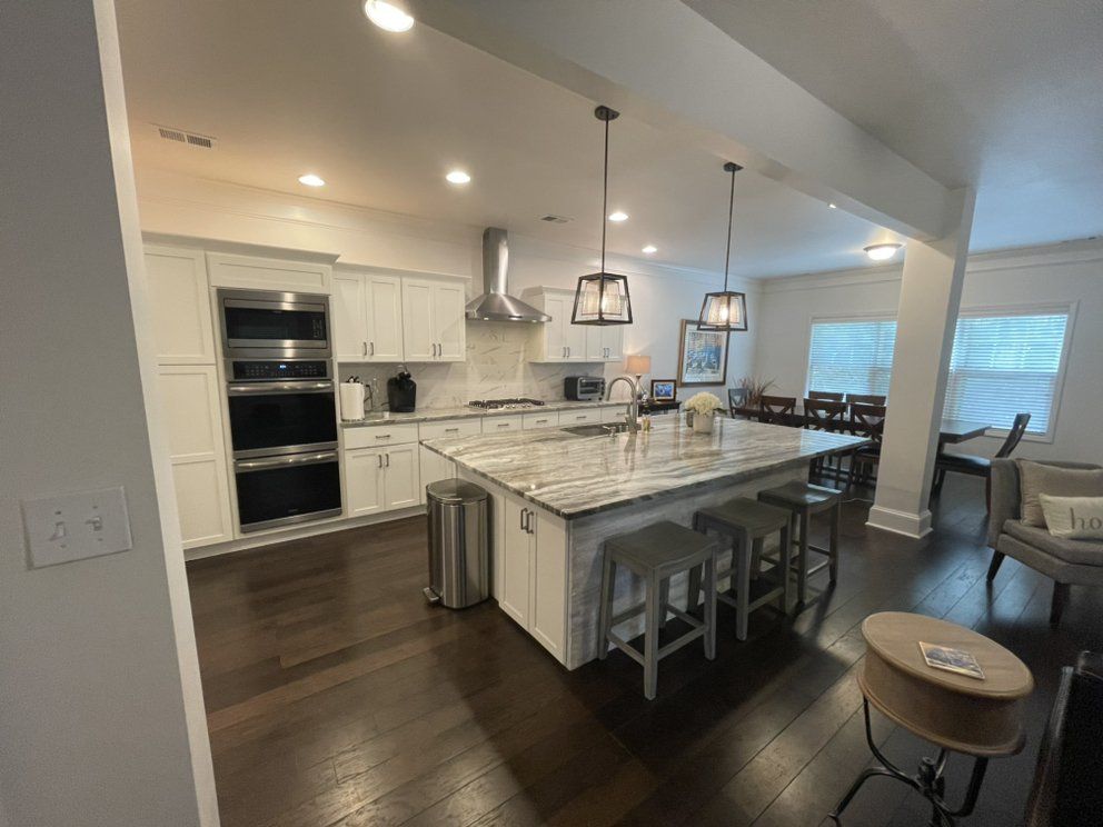 Modern white kitchen with large island, pendant lights, dark wood floors, and stools