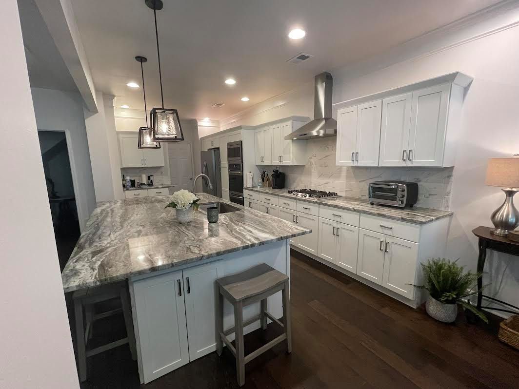 Bright kitchen with granite island, white cabinets, stainless range hood, pendant lights, and dark wood floors