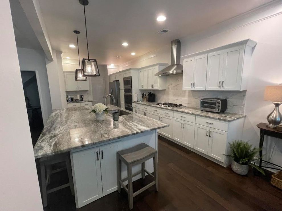 Modern kitchen with white cabinets, granite island, pendant lights, and dark wood floors