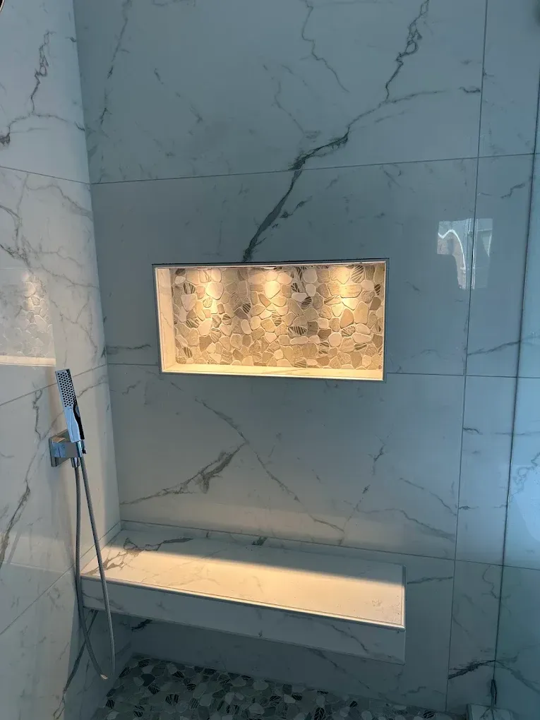 Marble-tiled shower with recessed lighted niche and built-in bench shelf
