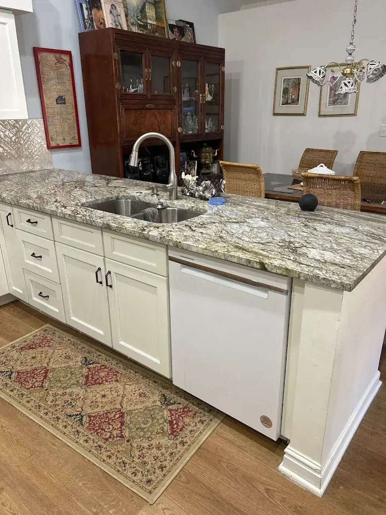 Granite kitchen island with sink, white cabinets, and a white dishwasher in a dining area