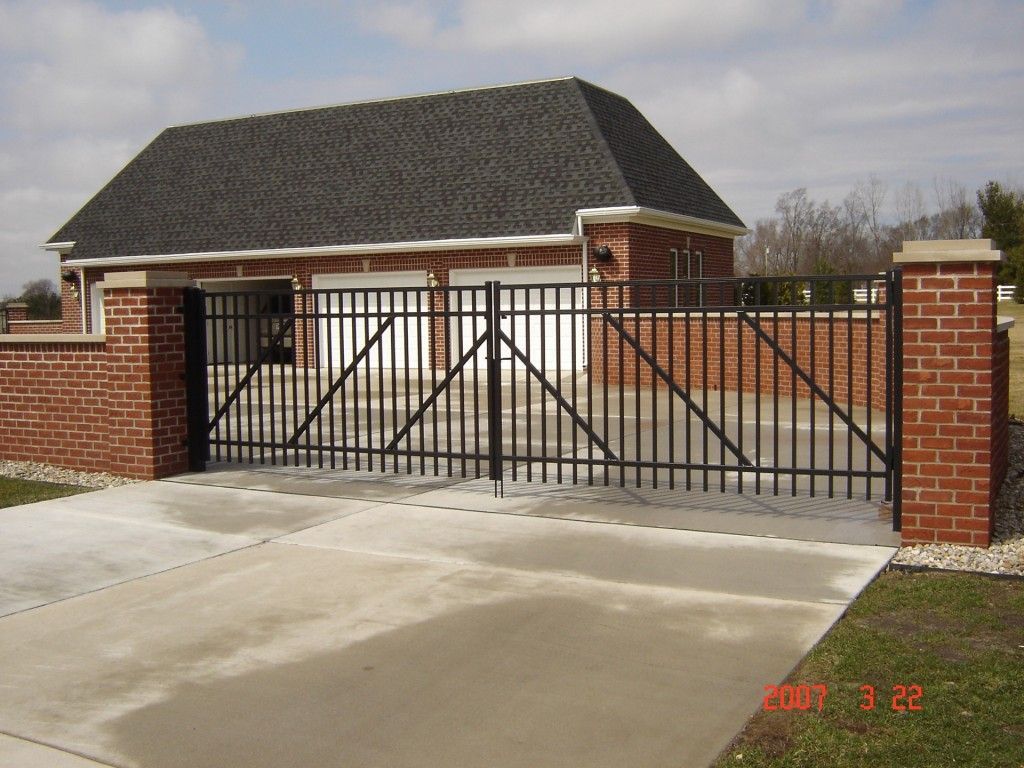 Black metal gate across a concrete driveway leading to a brick garage with a black roof.