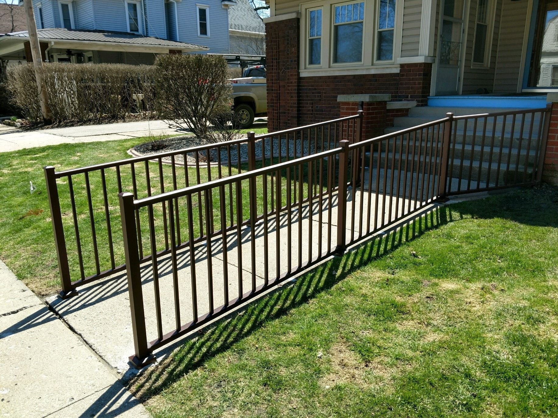 Brown metal ramp with railings leading to a brick home's entrance, set on grass.