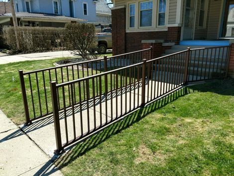 Brown metal ramp with railings leading up to a brick house with a porch and steps.