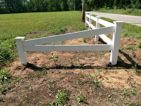 White wooden fence section on a grassy and dirt area, angled brace, sunny day.