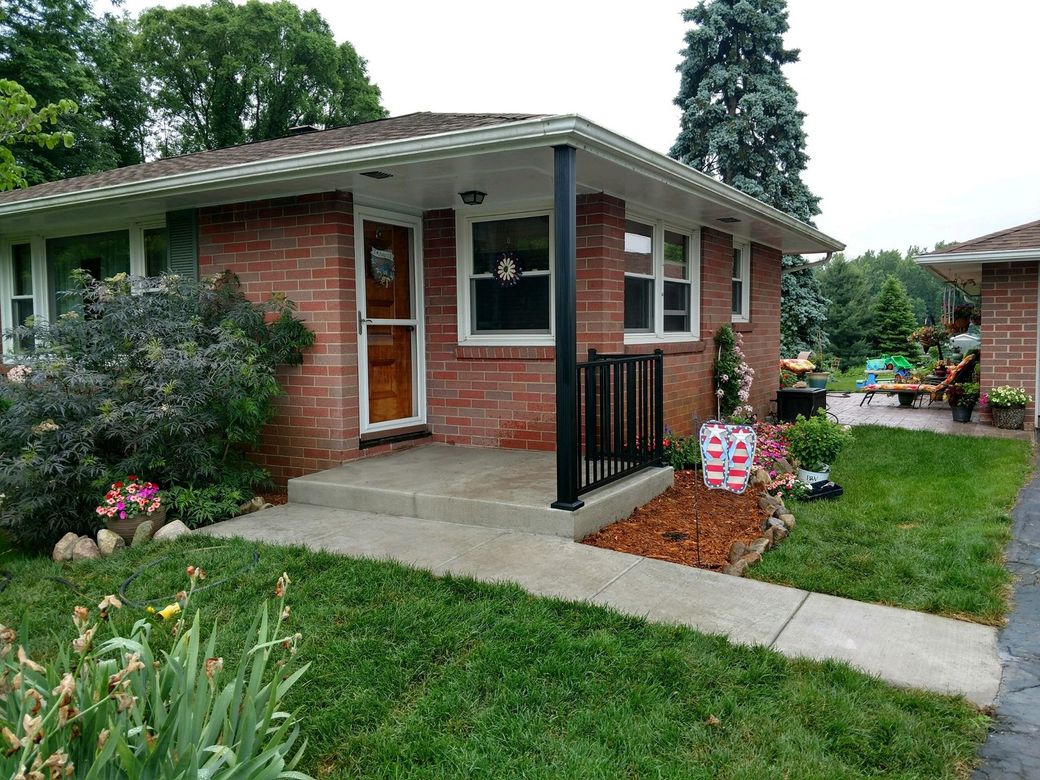 Brick bungalow with porch, black railing, and front yard landscaping.