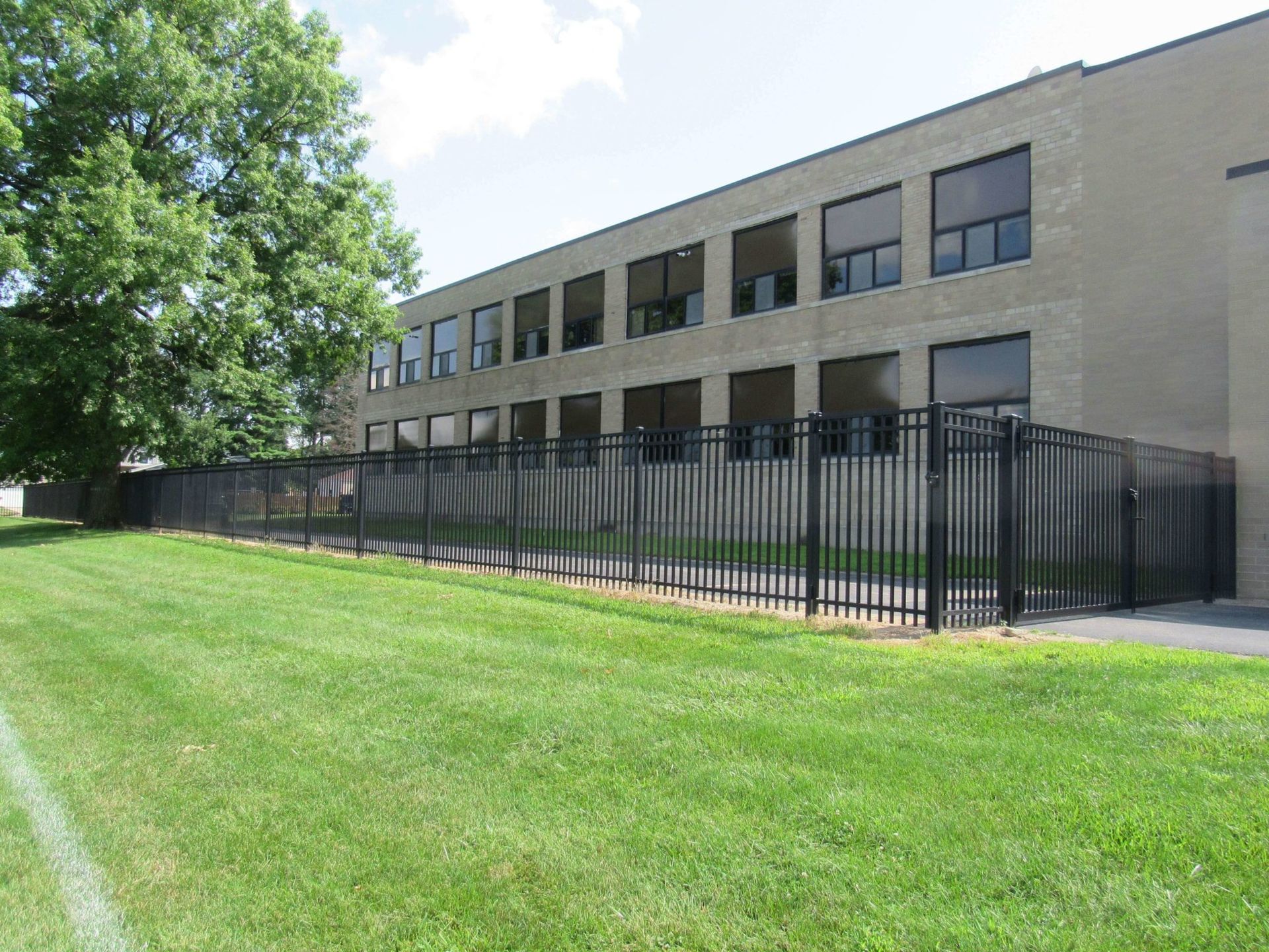 Exterior view of a beige brick school building with a black fence and green lawn.