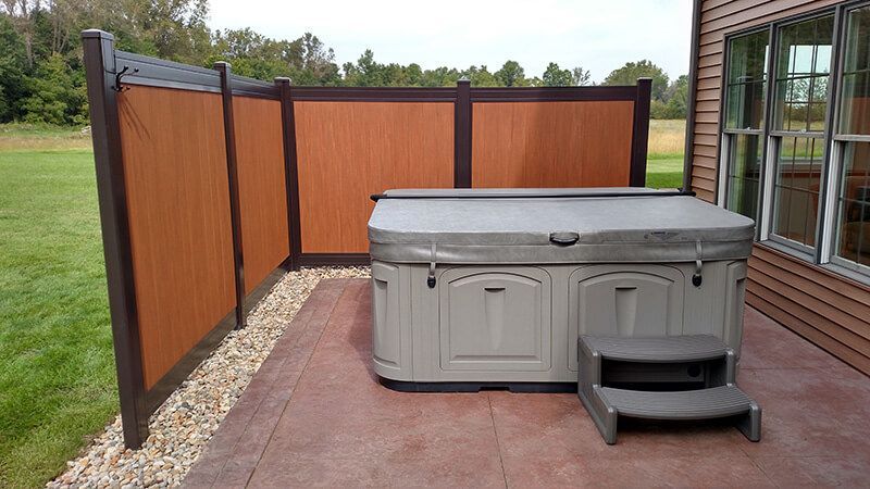 Hot tub on a patio, with privacy fence.  Gray hot tub with cover, brown fencing and a brown patio.