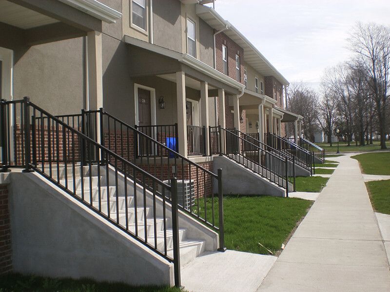 Row of townhouses with concrete steps, black railings, and a sidewalk.