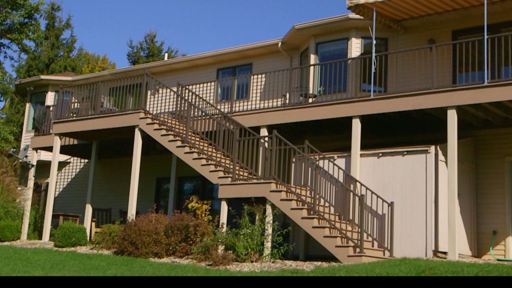 Two-story house with a wooden deck and staircase leading to the backyard, on a sunny day.