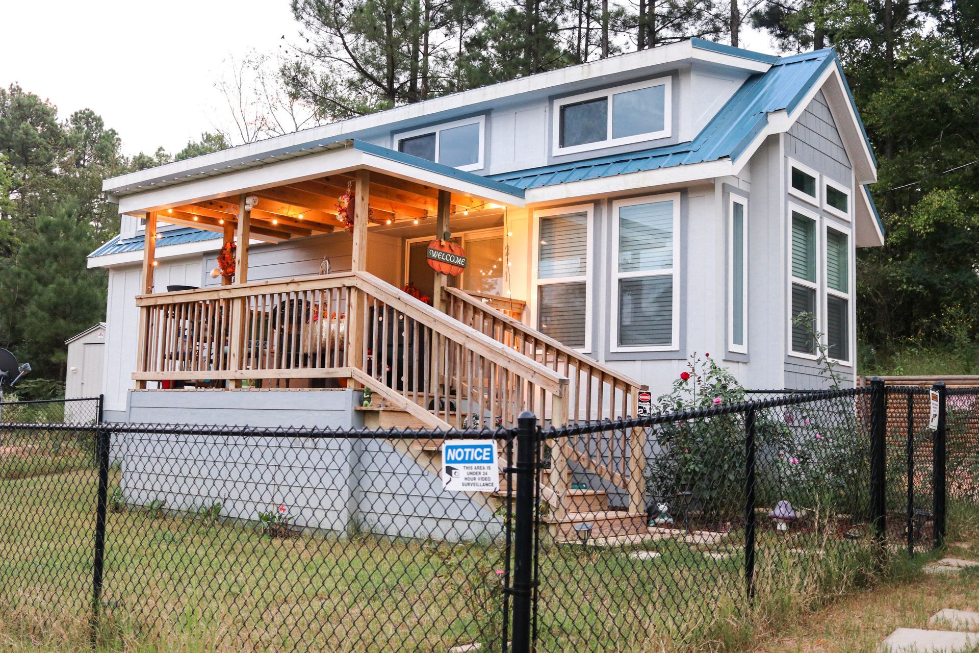 Small light blue house with a covered porch, wooden stairs, and a teal roof, behind a black fence.