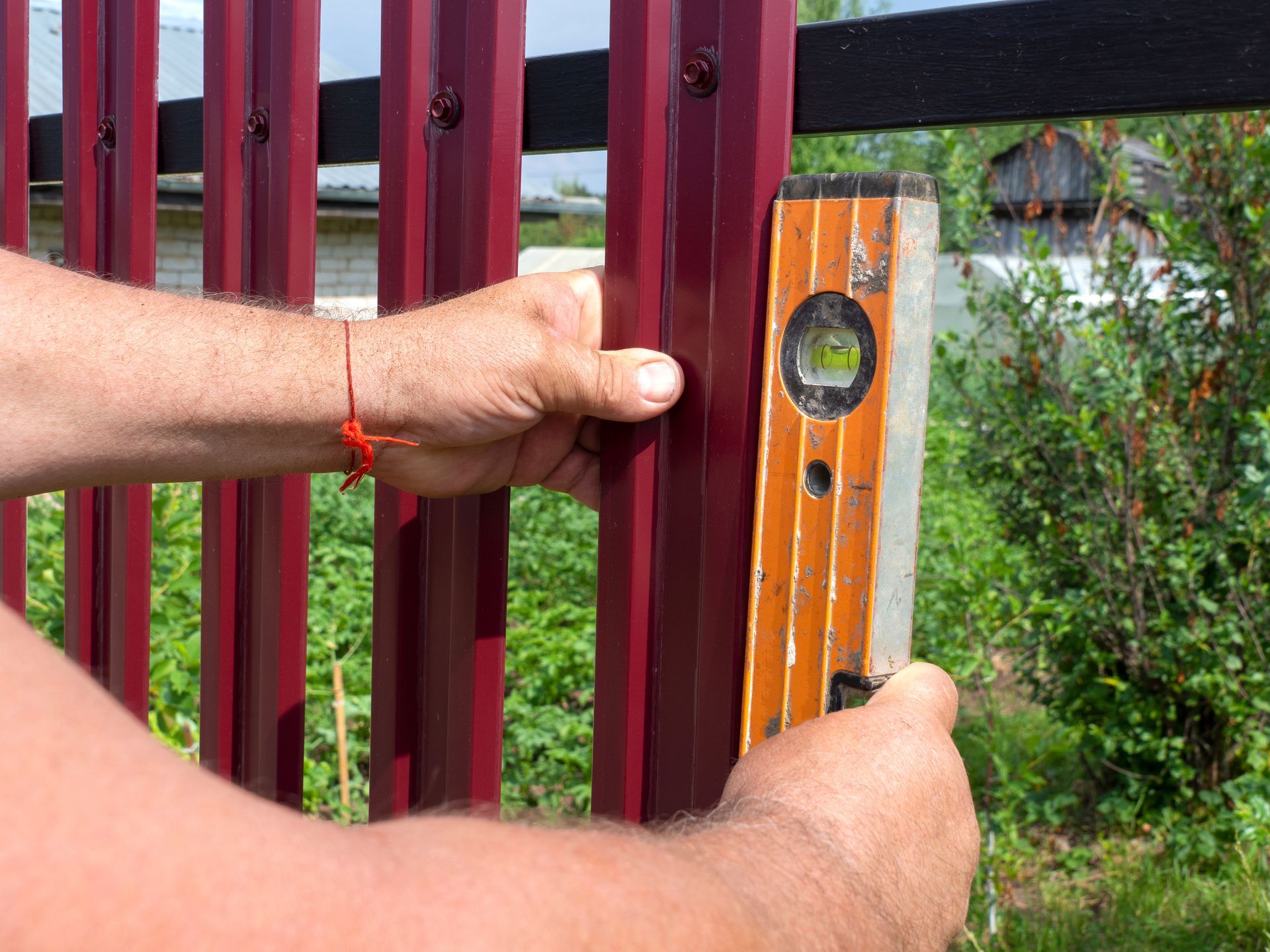 Person uses a level to check a burgundy metal fence post for plumb.