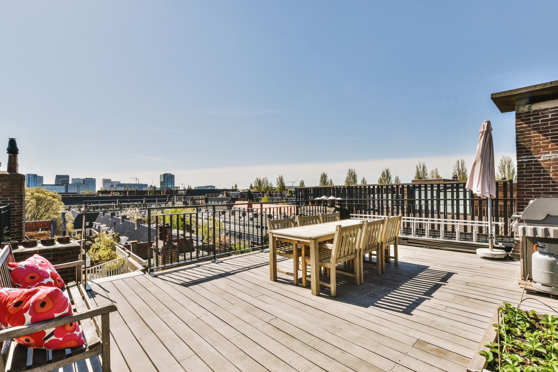 Rooftop deck with wooden furniture, overlooking a cityscape on a sunny day.