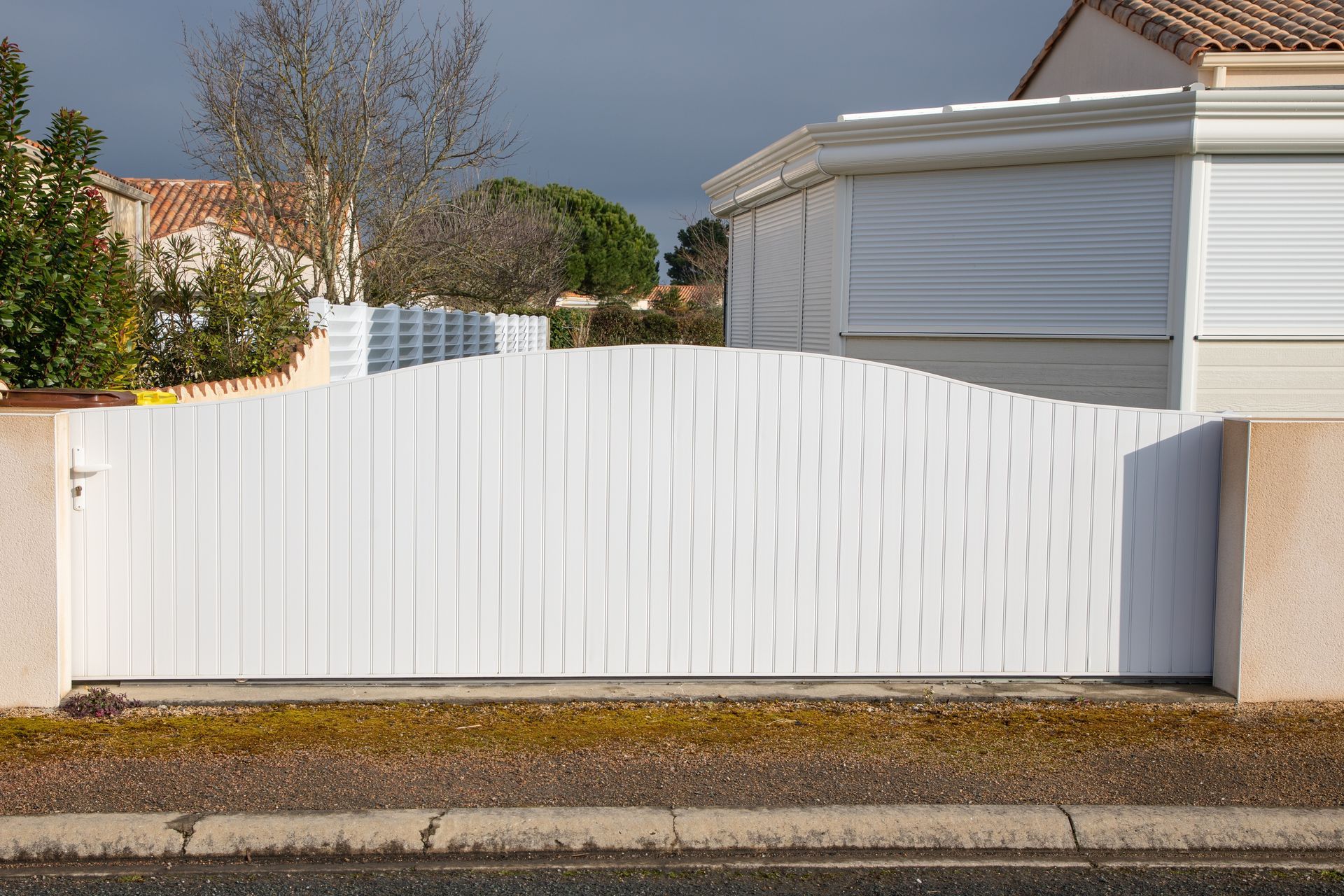 White wooden gate with a curved top, set between beige pillars on a street.
